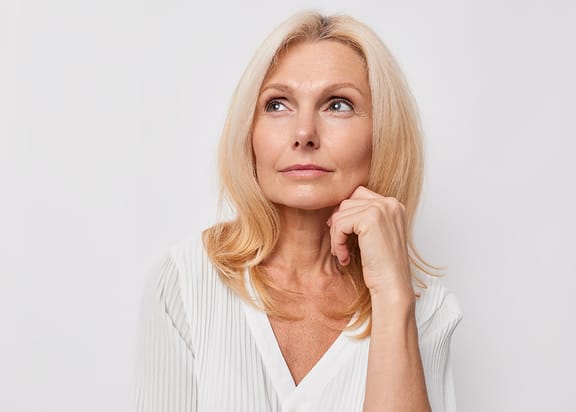 Mature blond woman with hand on face thinking