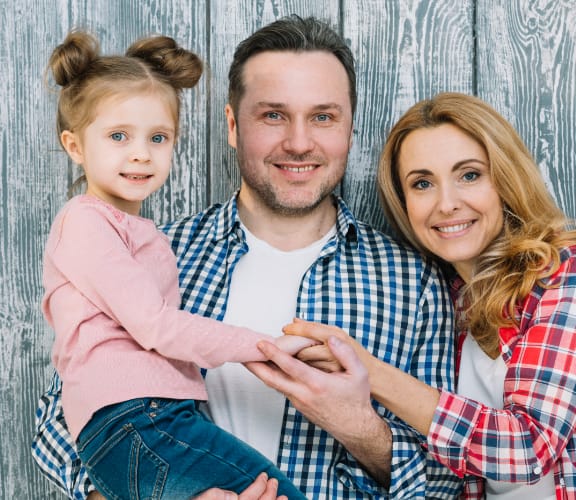 Family of three standing in front of a wooden wall